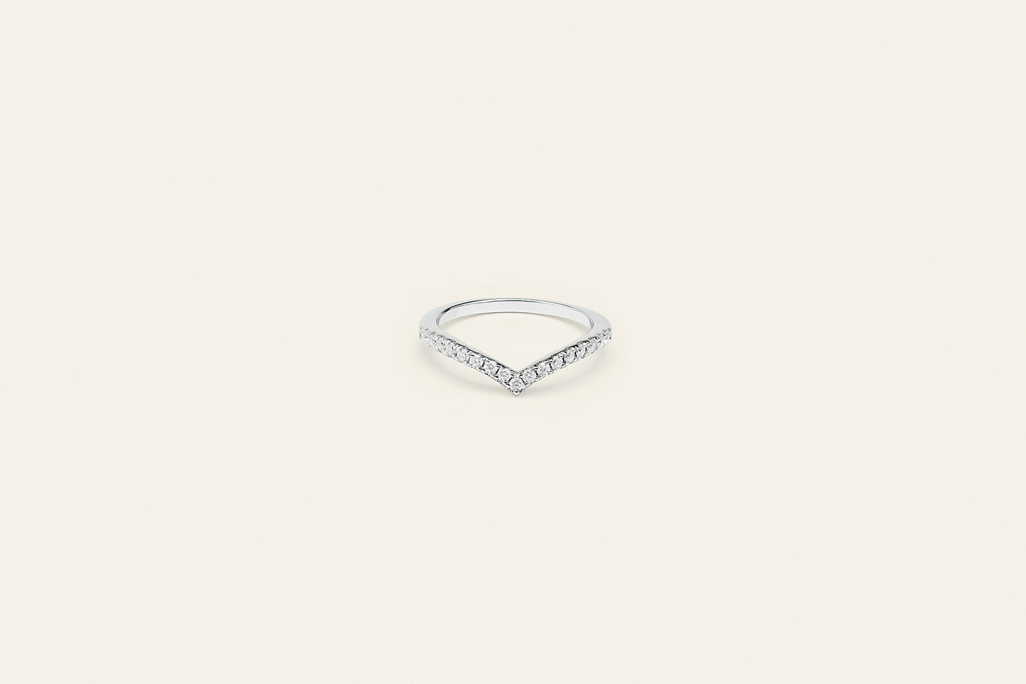 En silverring med klara moissanite stenar på framsidan. Ringen har en v-design och är placerad mot en ljusbeige bakgrund.