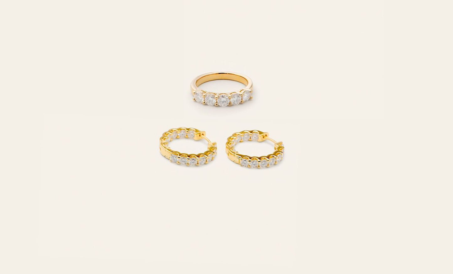 Vackert smyckesset i guld som består av ett par hoop örhängen i guld och en guldring. Örhängena och ringen har skinande stenar på sig.