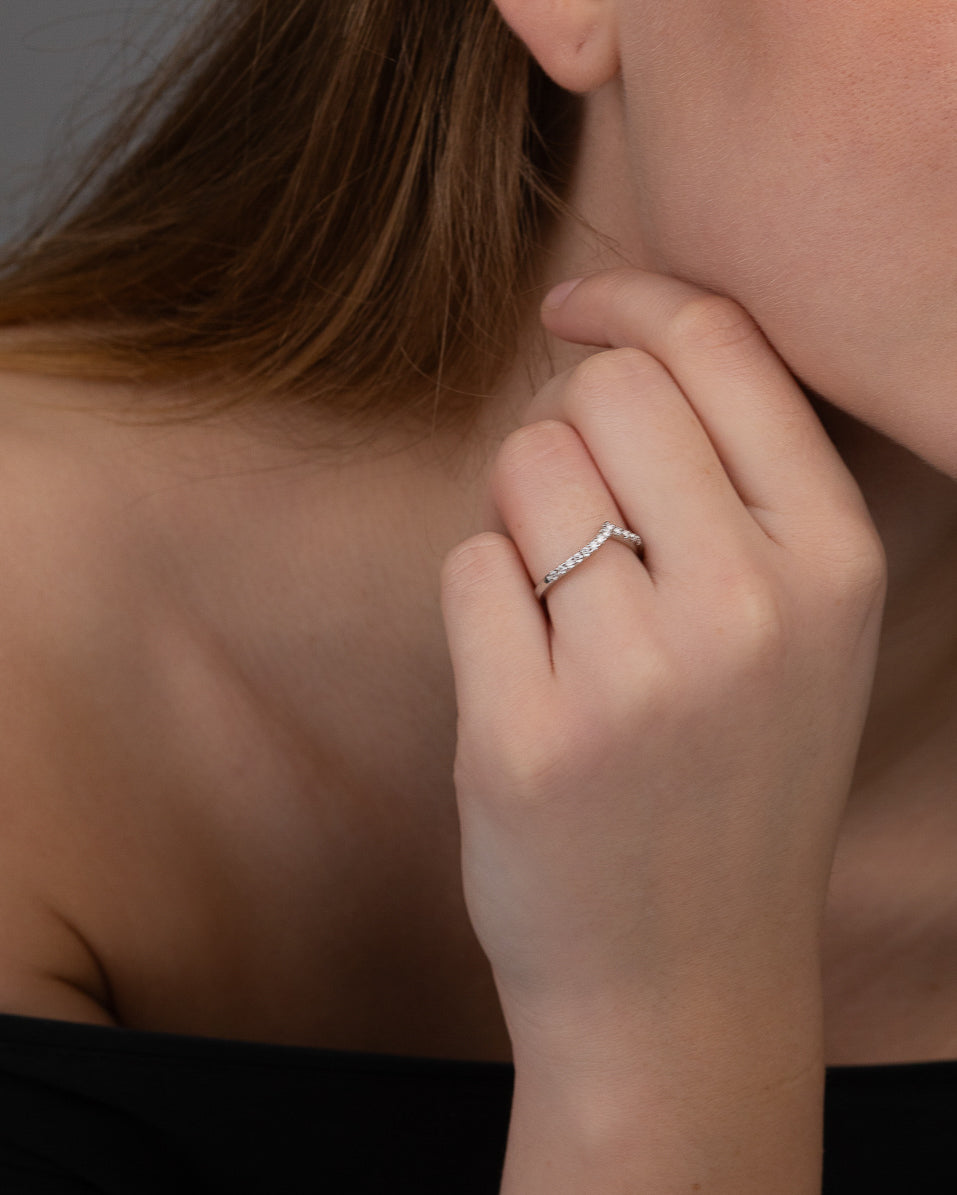 En handmodell som bär en v-formad silverring med silverstenar på framsidan.