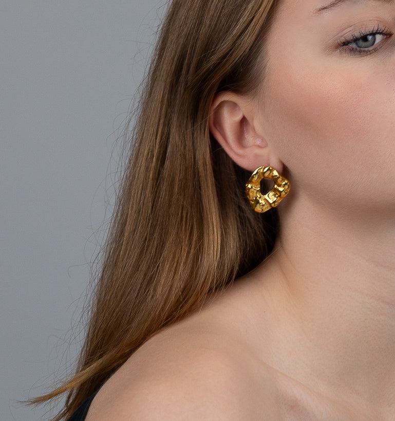 A model wearing chunky gold earrings with a molten gold design shaped as oval rings.
