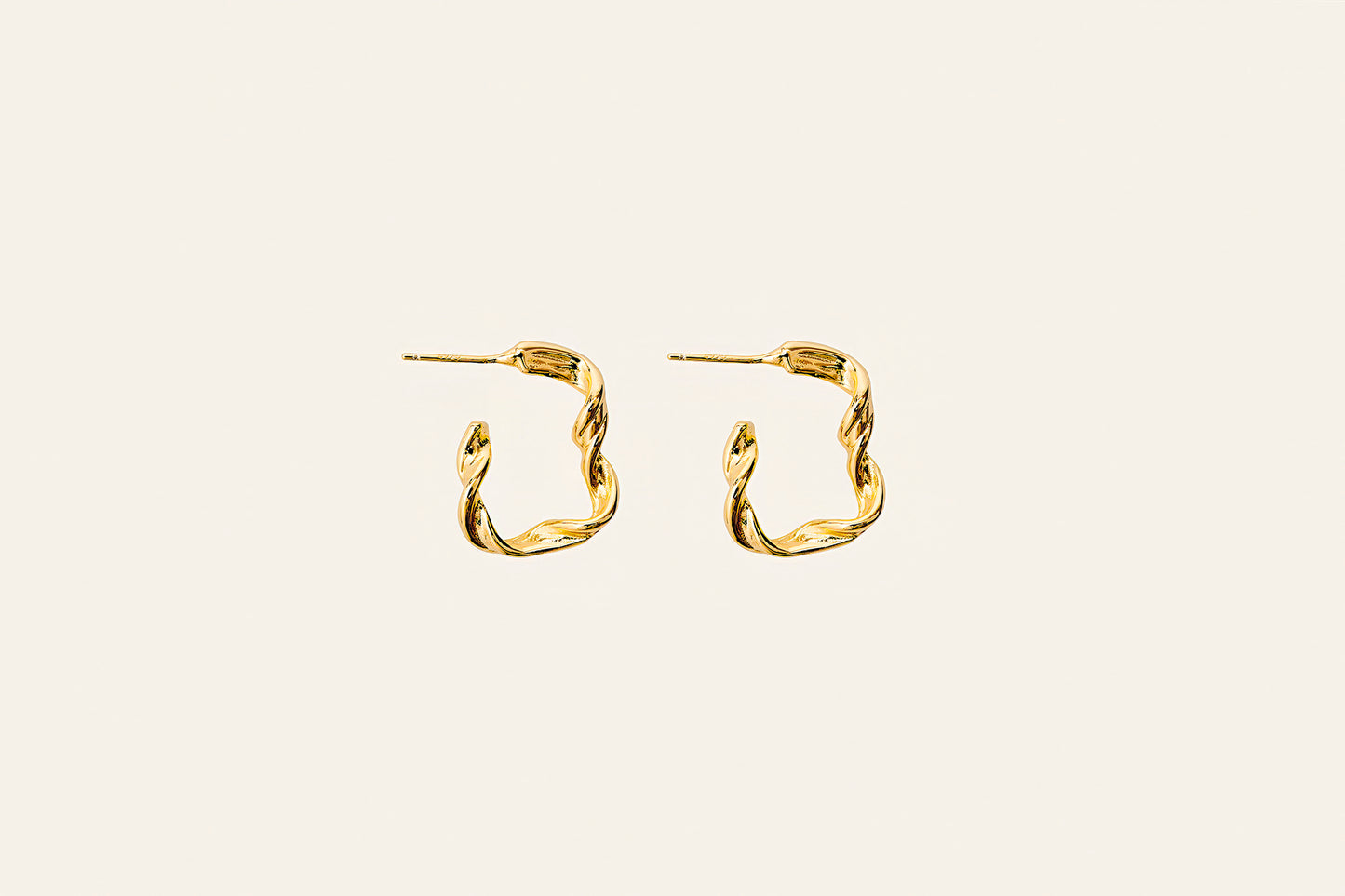18k eleganta guldörhängen med en smal twistdesign placerade på en ljus beige bakgrund. stilrena och eleganta