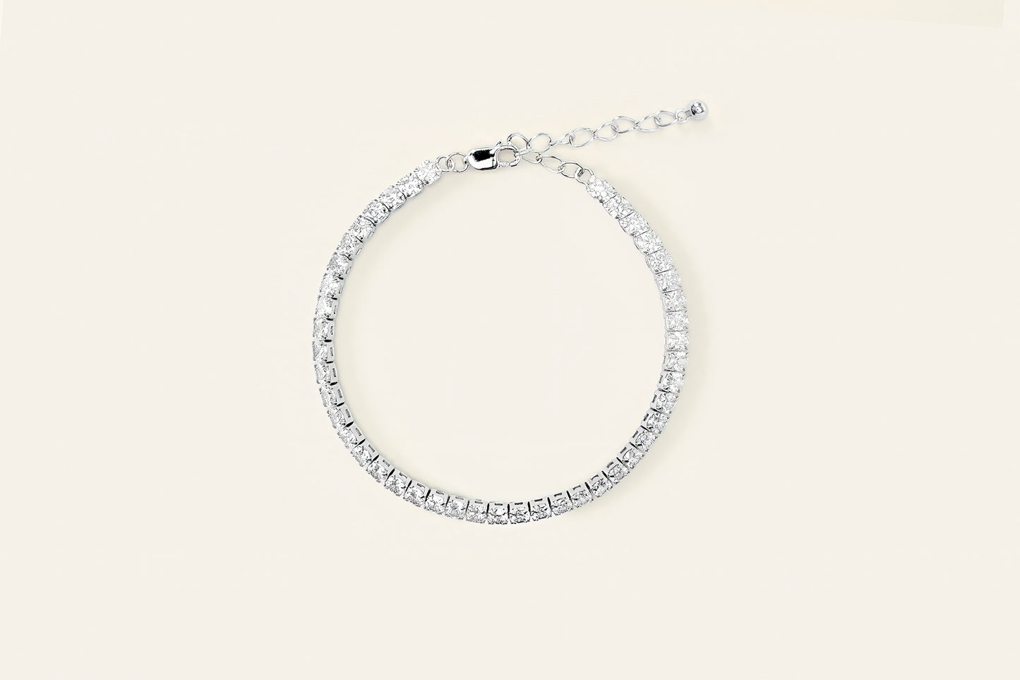 Ett elegant tennisarmband i silver täckt av glansiga stenar, placerat mot en ljusbeige bakgrund.
