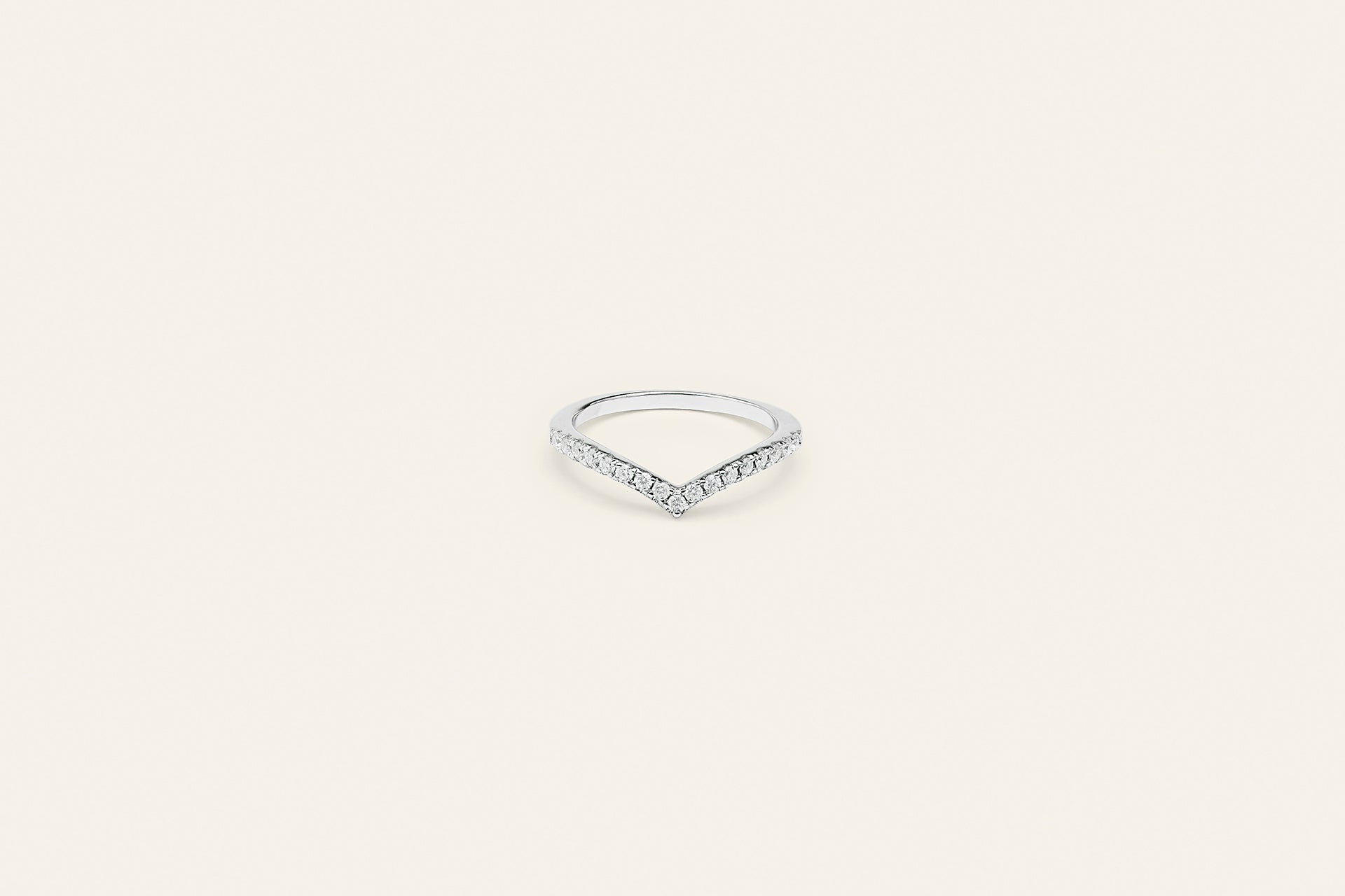 En silverring med klara moissanite stenar på framsidan. Ringen har en v-design och är placerad mot en ljusbeige bakgrund. 