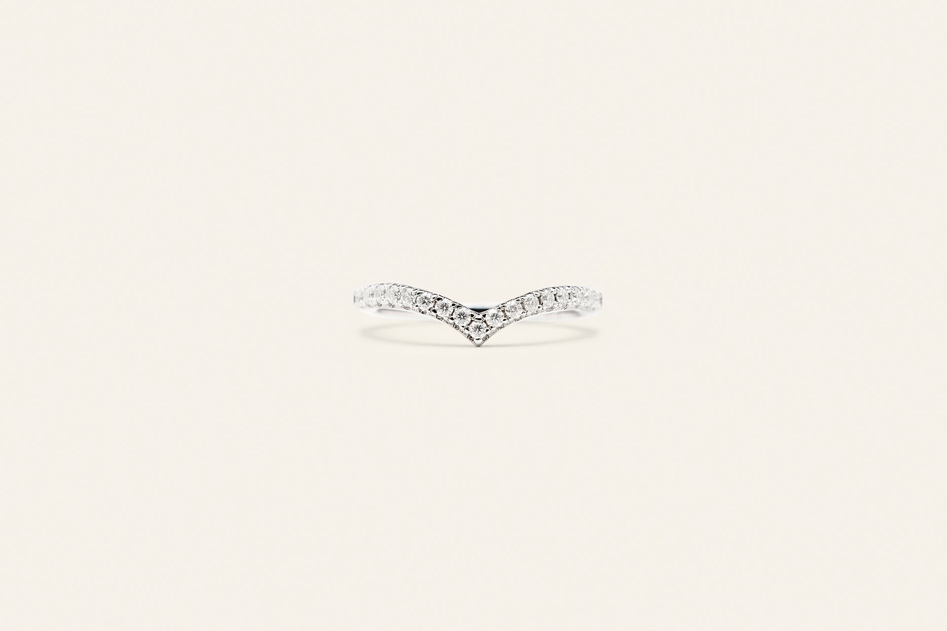 Elegant och tidlös silverring med en V-formad design. Ringen har silverstenar på framsidan och är placerad mot en ljusbeige bakgrund. 